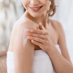 Une femme souriante dans une serviette tenant une crème sur son bras